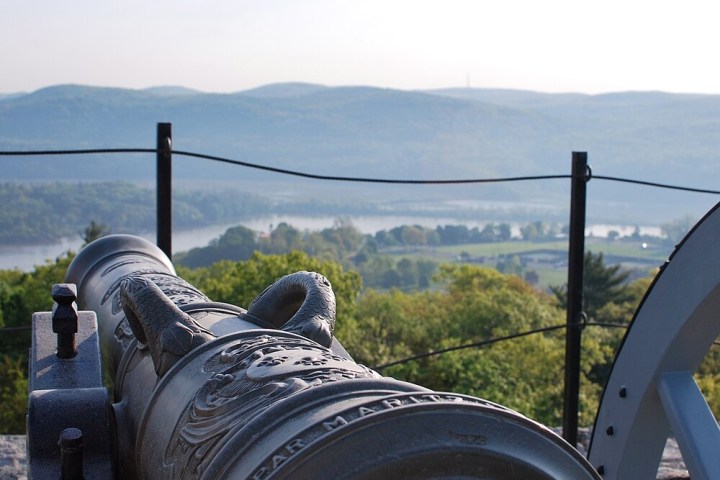 Historic cannon overlooking a scenic valley with hills, river, and trees in the background.